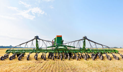 Agricultural seeder against the background of a wide field on yellow stubble and a blue cloudy sky.