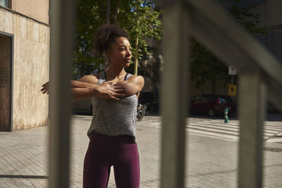 Sportswoman stretching on sunny day seen through fence