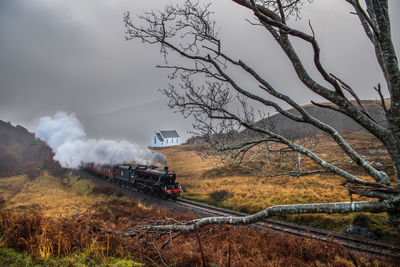 Steam train amidst field against sky