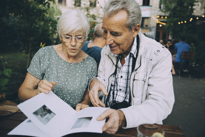 Senior man and woman tourist looking at pictures in book while sitting in restaurant