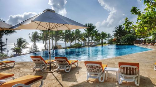 Lounge chairs and tables at beach against sky