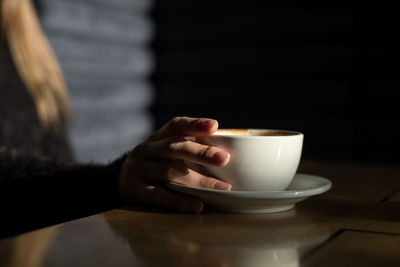 Close-up of hand holding coffee cup on table