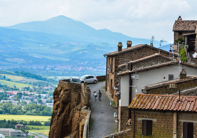 People walking on road by houses against mountains