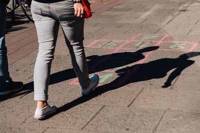Low section of woman walking towards hopscotch on footpath