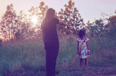 Rear view of women standing on field against trees