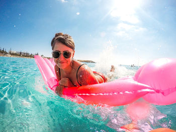 Portrait of woman floating on pink pool raft in sea