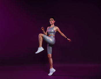 Full length of young woman jumping against black background