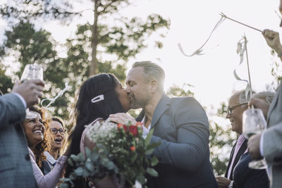 Newlywed couple kissing on mouth by guests cheering them at wedding ceremony