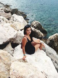 Portrait of young woman standing on rock by sea