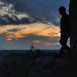 Silhouette man standing on rock against sky during sunset