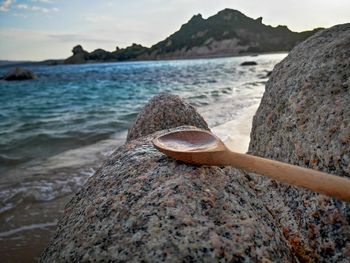 Close-up of rusty metal on rock at beach against sky