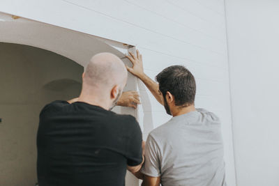 Rear view of men attaching wood on wall