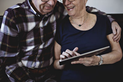 Midsection of smiling senior couple sitting while sharing digital tablet at home