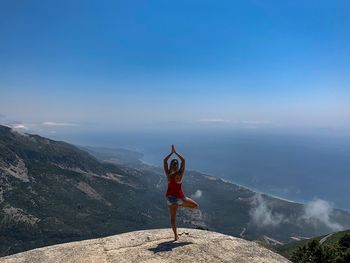 Rear view of woman standing on one leg over mountain against sky