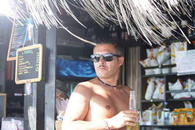 Portrait of shirtless man wearing sunglasses standing outdoors