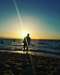 Silhouette men standing on beach against sky during sunset