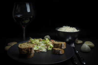 Close-up of fresh healthy meal served with wine against black background