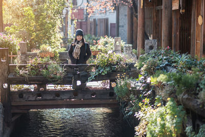 Portrait of young woman standing on bridge against plants