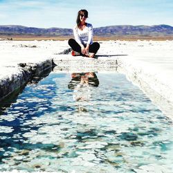 Young woman sitting in water against sky