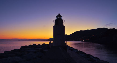 Lighthouse by sea against sky during sunset