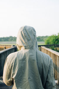 Rear view of person wearing hooded shirt while standing against clear sky