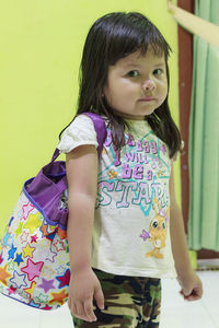 Cute girl looking away while standing against wall