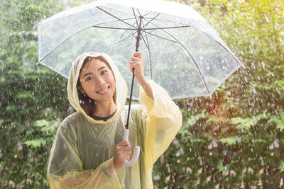 Portrait of woman with umbrella standing against trees during rainy season