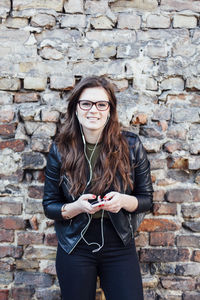 Portrait of smiling young woman using phone while standing against wall