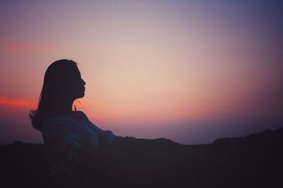 Silhouette woman sitting against sky during sunset