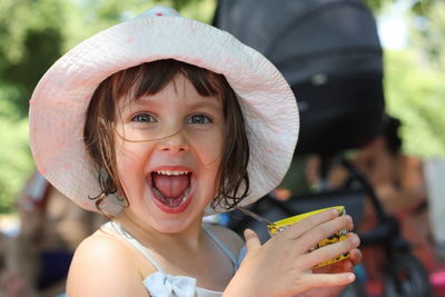 Close-up portrait of happy girl with mouth open holding container while standing outdoors