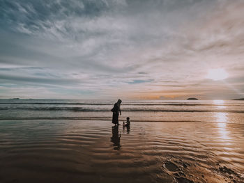 People on beach against sky during sunset