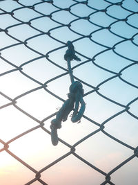 Low angle view of rope tied on chainlink fence against sky