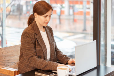 Young woman using laptop while standing in office