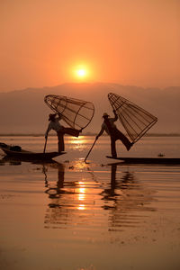 Men fishing in lake at sunset