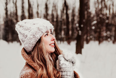 Woman standing on the white snow in winter forest. girl is smiling and happy with closed eyes