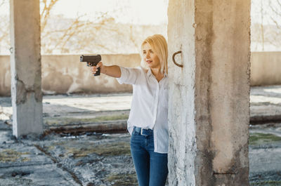 Woman holding gun while standing amidst columns