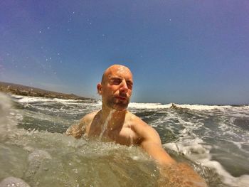 Portrait of shirtless man in sea against sky