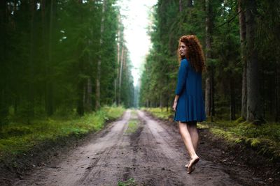 Full length of woman walking on road amidst trees at forest