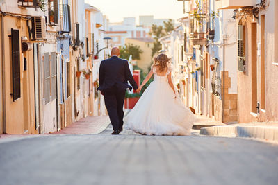 Rear view of friends walking on street amidst buildings