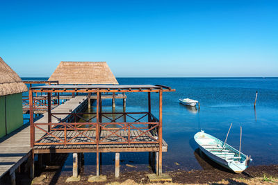 Boat moored by pier against clear blue sky during sunny day