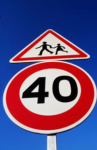 Low angle view of speed limit and pedestrian signboard against blue sky