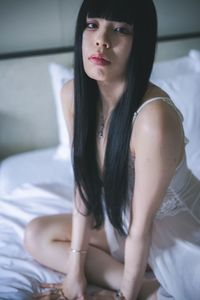 Young woman looking away while sitting on bed