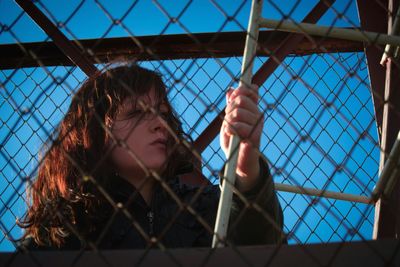 Low angle view of woman seen through chainlink fence