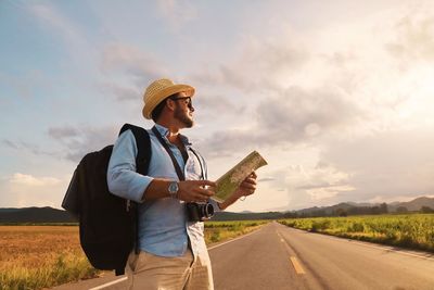 Man holding luggage standing on road against sky