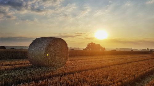 Hay bales on field against sky during sunset