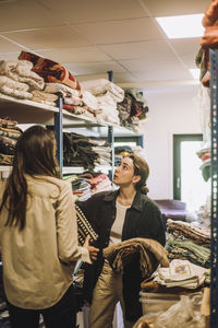 Female fashion designers talking while standing near rack at workshop