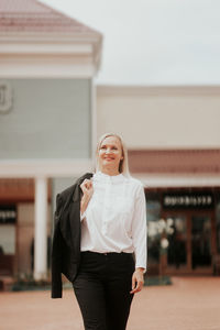 A confident smiling businesswoman in a white shirt and business suit walking along the street