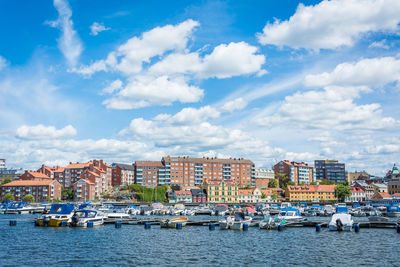 Sailboats moored on sea by buildings against sky