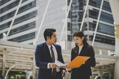 Business people discussing file while standing against building in city