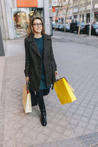 Woman walking on sidewalk holding shopping bags